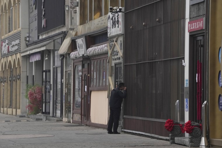 A security guard peers into a store along a stretch of shuttered restaurants in Beijing on Thursday. Beijing and Zhengzhou are in near-lockdown with schools, parks and shopping malls closed.