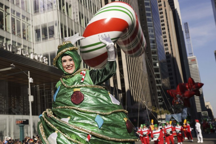 A parade performer in a Christmas Tree leads a giant candy cane down Sixth avenue. 