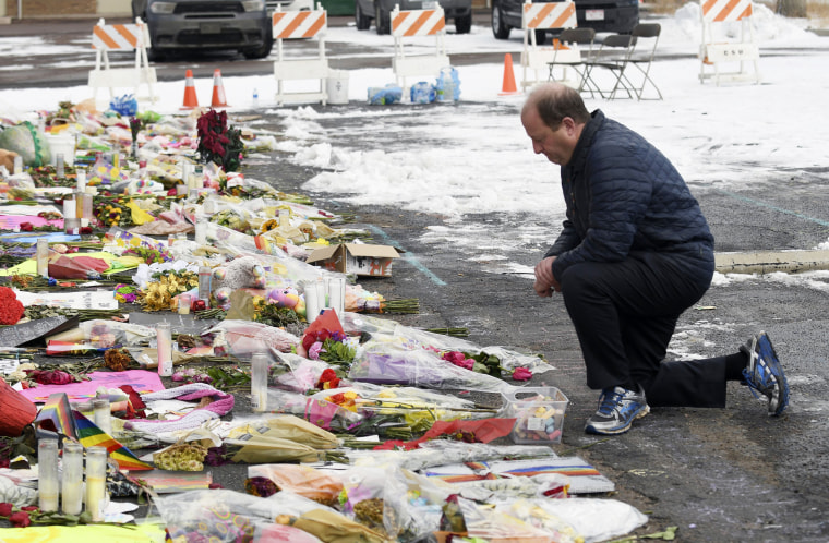 Gov. Jared Polis kneels in front of a memorial set up outside Club Q