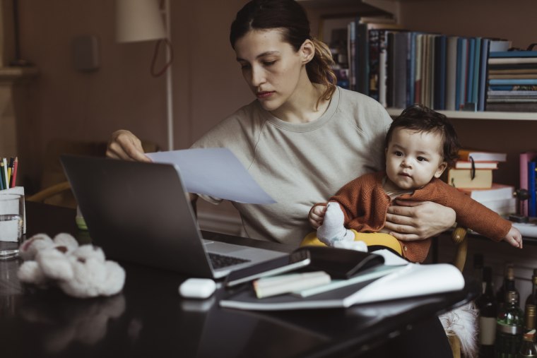 Una mujer revisa las facturas mientras sostiene a su bebé.
