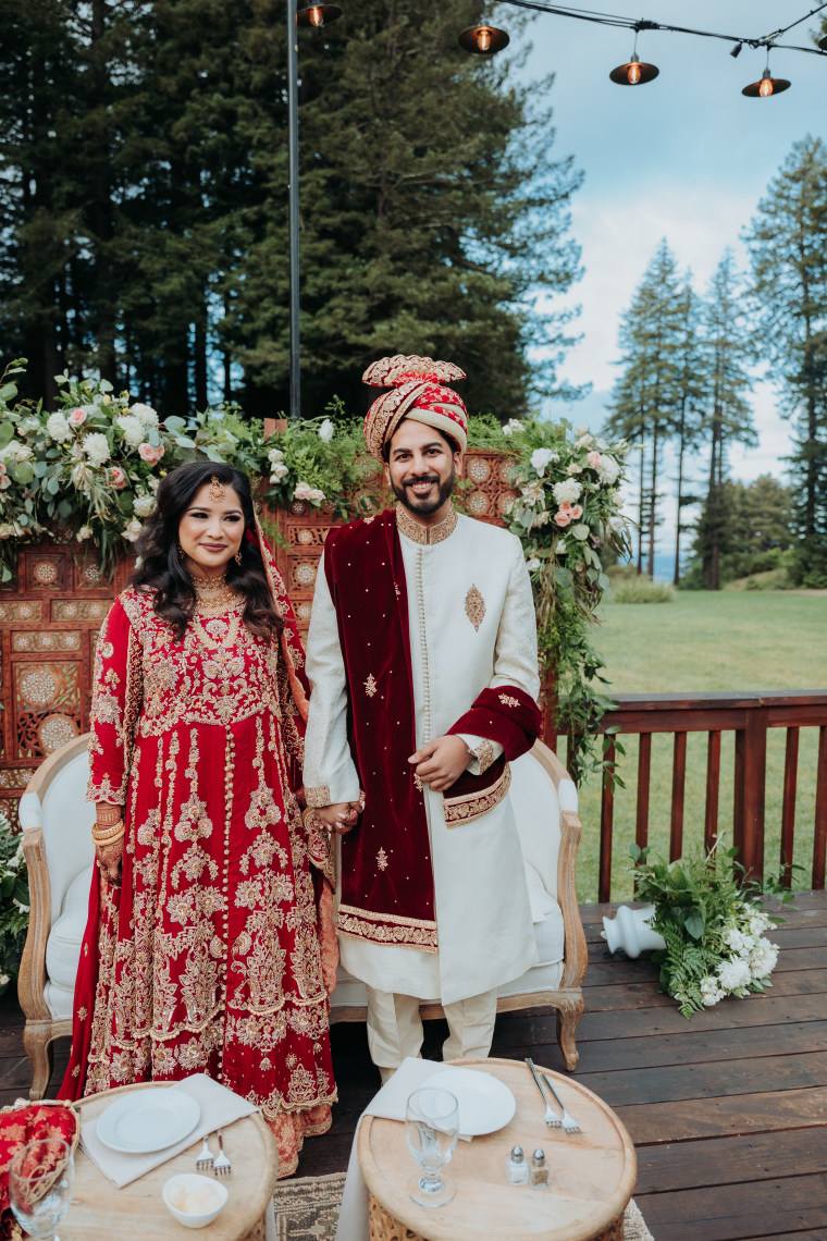 Bride and groom dressed in red and white standing in front of flowers