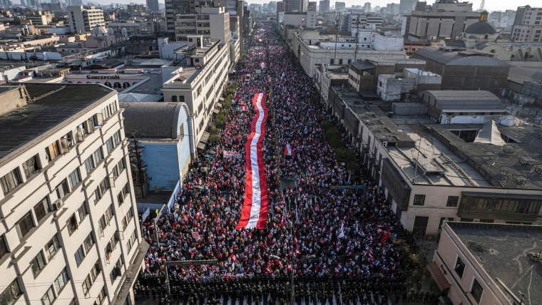 En una toma aérea se ven centenares de personas sobre una gran avenida en Lima ondeando una bandera de Perú 