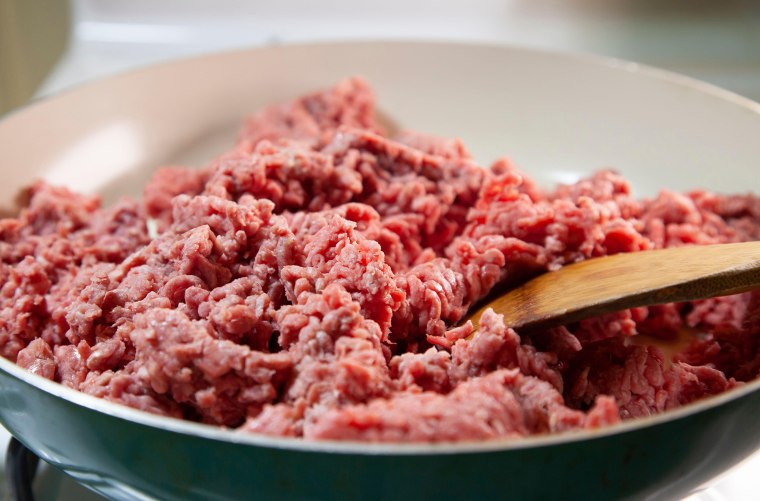 Close up of a wooden spoon in raw ground beef in a frying pan