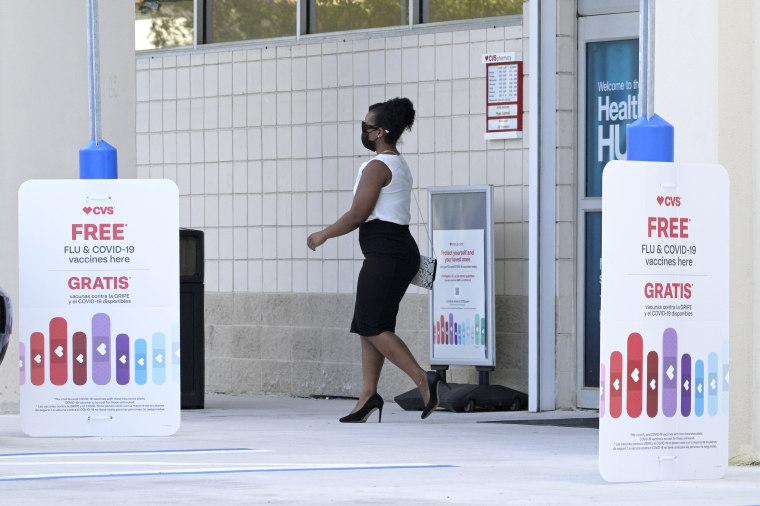 A woman walks past signs advertising free flu shots and COVID-19 vaccines