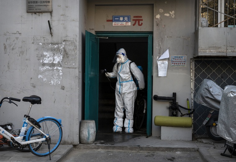 An epidemic control worker wears PPE as he disinfects a doorway in a neighborhood that recently was in lockdown due to COVID-19 cases and has now opened