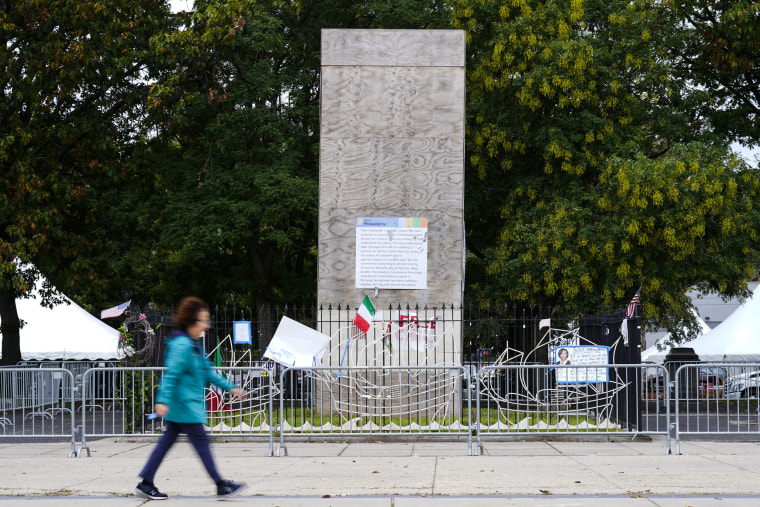 A pedestrian walks by an encased statue of Christopher Columbus at Marconi Plaza