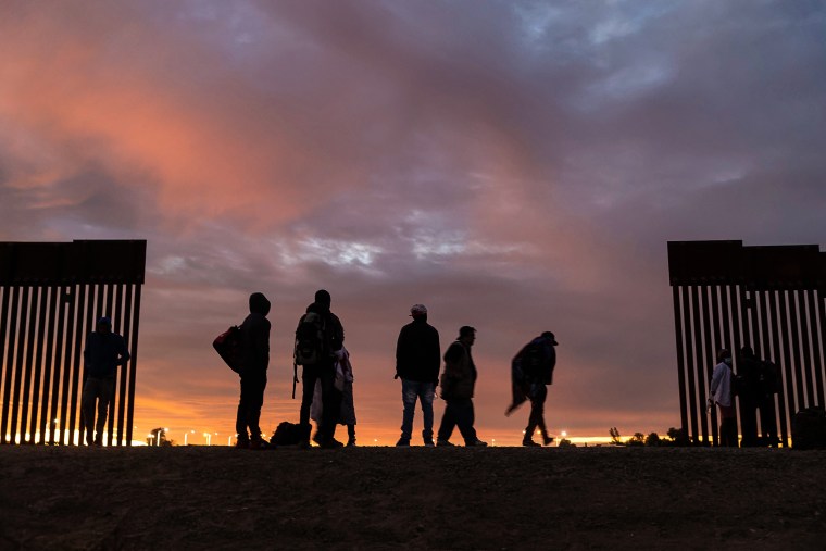 People from Haiti stand at a gap in the U.S.-Mexico border wall after having traveled from South America to the United States on Dec. 10, 2021 in Yuma, Ariz.