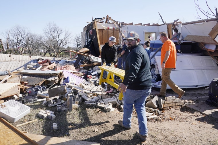 Adam Lee, left, and Jr. Ibarra, right, carry a table from a friend's home after it was destroyed by a tornado, on Dec. 13, 2022, in Wayne, Okla. 