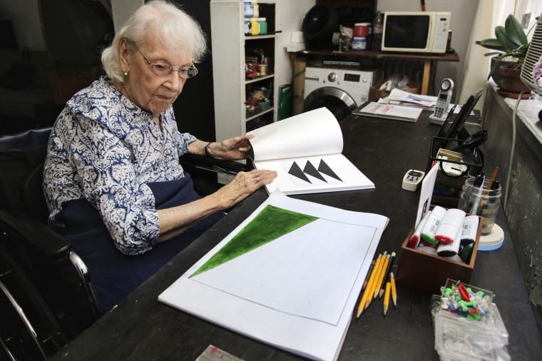 Carmen Herrera looks at a sketch for one of her paintings as she leafs through a gallery catalogue of some of her work in her New York studio on May 29, 2015.