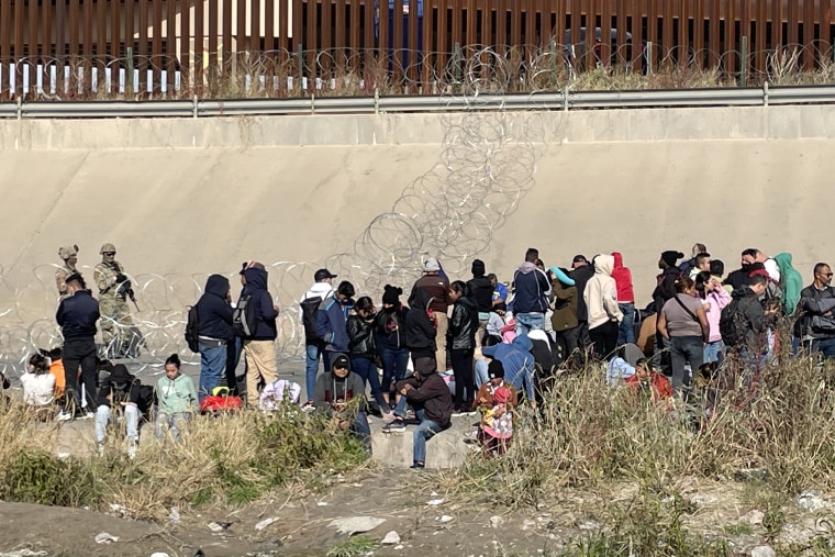 Three migrants who had managed to evade National Guard and cross the Rio  Grande onto U.S. territory wait for Border Patrol along a wall set back  from the geographical border, in El