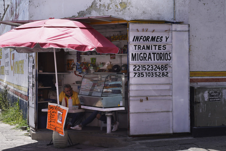 An empanada vendor's stall advertises information, and immigration documents outside the main immigration office in Puebla, Mexico,