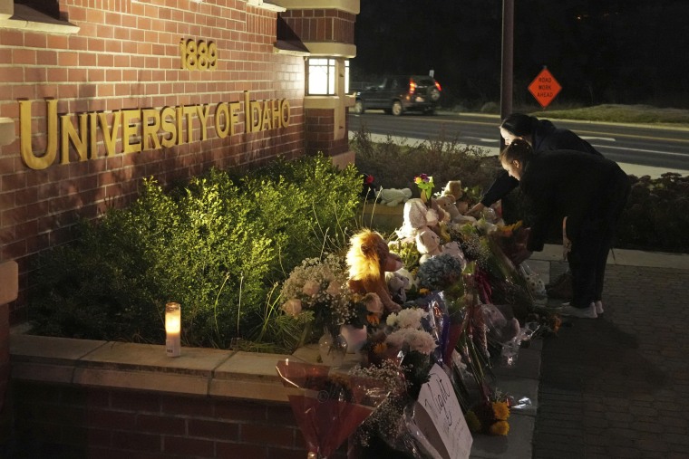 People place flowers on a monument in front of an entrance sign to the University of Idaho campus