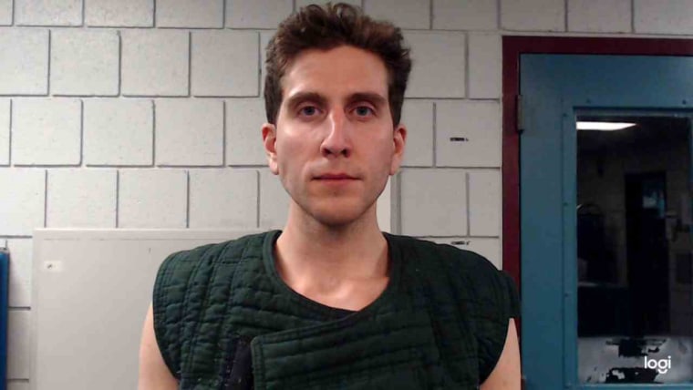 Kohberger in a dark green vest for his mug shot in front of cinderblock walls and a blue door.