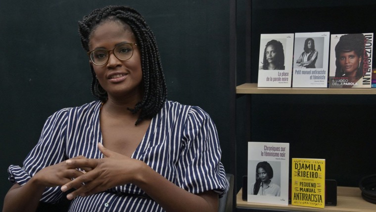 La autora y filósofa afrobrasileña Djamila Ribeiro, con anteojos, posa frente a copias en portugués y francés de sus libros durante un evento en São Paulo de 2021