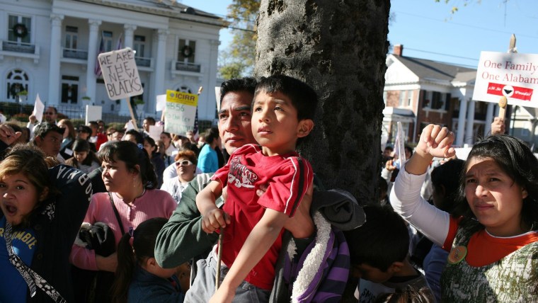 Durante una protesta en Alabama, un padre latino levanta en hombros a su hijo quien trae una camisa color rojo
