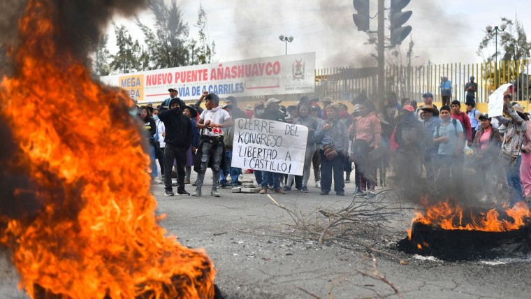 Un grupo de peruanos protesta frente a llantas a las que les prendieron fuego. Uno sostiene una pancarta que dice "Cierre del Congreso y libertad a Castillo" en referencia a Pedro Castillo, quien fue removido el 7 de diciembre y enfrenta cargos de rebelión.