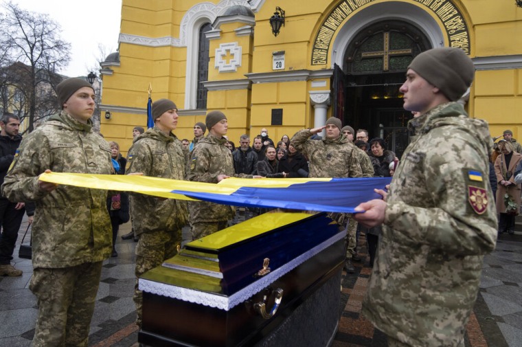 Militares ucranianos sostienen una bandera sobre el ataúd de un compañero muerto en un campo de batalla con las fuerzas rusas. 