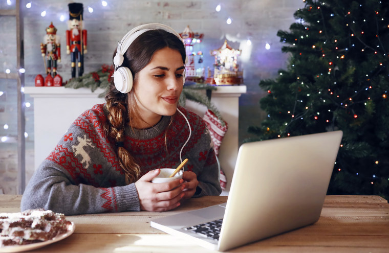 Woman with cup of coffee using laptop and headphones at Christmas time.