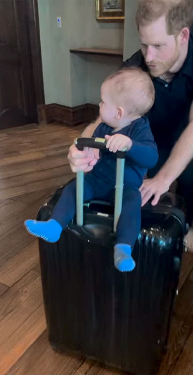 Harry is seen pushing one of his children around on a rolling suitcase.