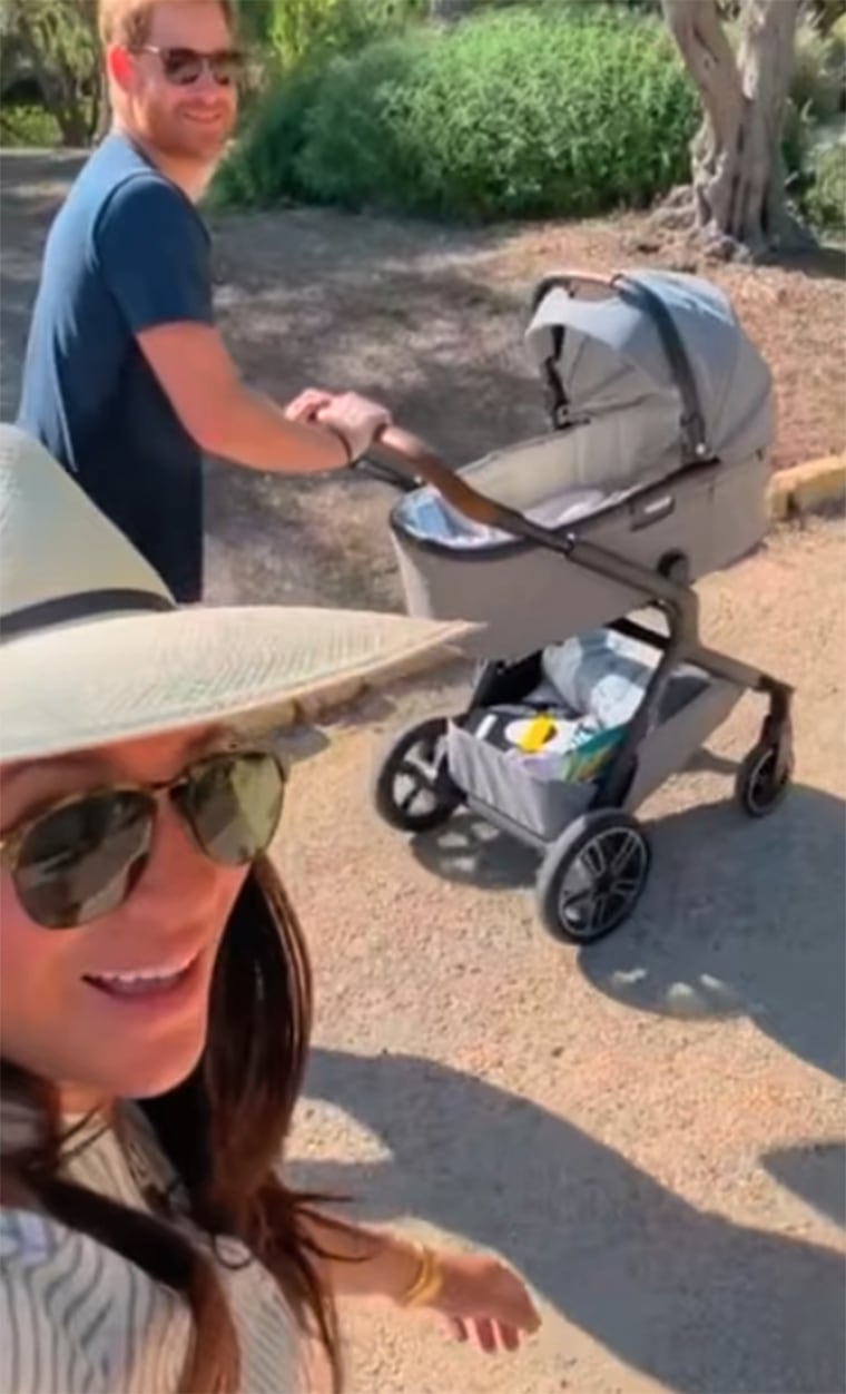 Harry is seen pushing a stroller while Meghan takes a selfie in this sweet family moment.