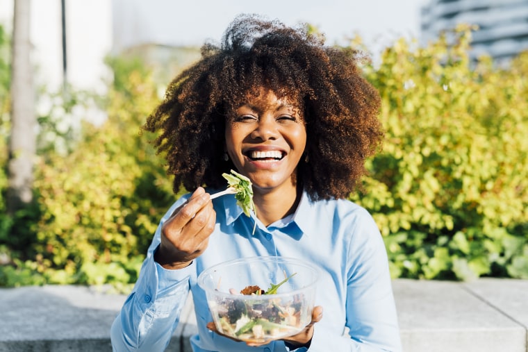 Happy businesswoman eating salad on sunny day