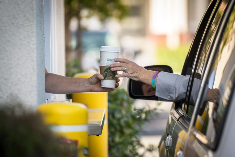An employee passes a drink order to a customer at the drive-thru of a Starbucks Corp. coffee.
