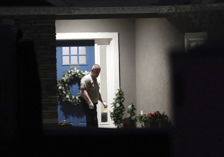 A law enforcement officer stands near the front door of the Enoch, Utah home where eight family members were found dead from gunshot wounds.