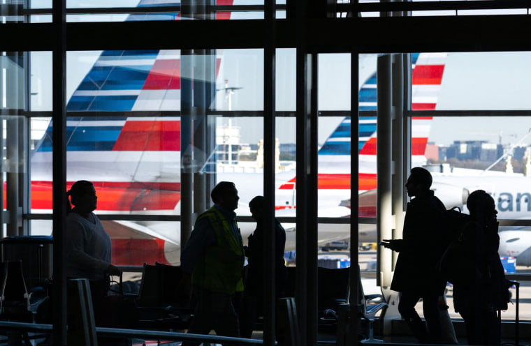 People walk past a window overlooking American Airlines airplanes
