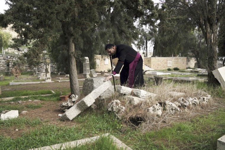 Palestinian Anglican bishop Hosam Naoum touches a vandalized grave at a historic Protestant Cemetery