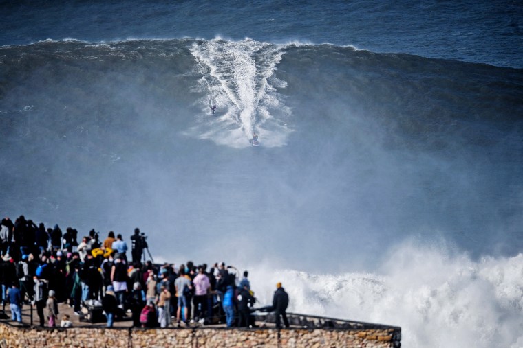 Spectators watch as a surfer is towed by a jet ski in a wave at Praia do Norte in Nazare, Portugal, on Feb. 25, 2022.