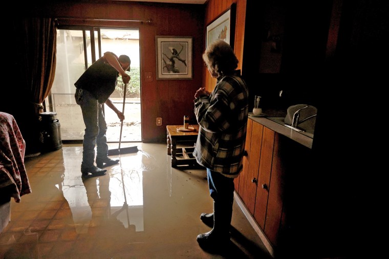 Lana Spurlock, right, looks on as Dakota Boone sweeps water out of her flooded home on Jan. 11, 2023 in Planada, Calif.