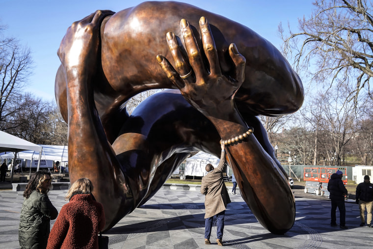A man reaches to touch a detail of the 20-foot-high bronze sculpture "The Embrace," a memorial to Dr. Martin Luther King Jr. and Coretta Scott King, in the Boston Common on Jan. 10, 2023, in Boston.