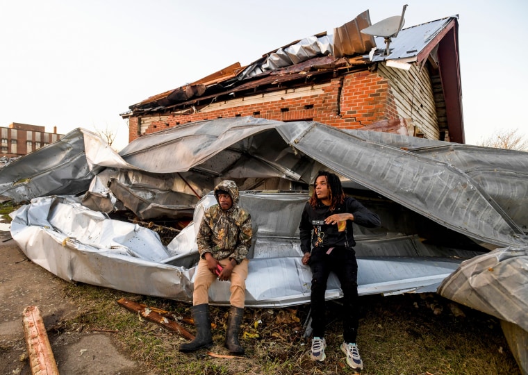 Cordel Tyus, left, and Devo McGraw sit on the exploded roof of an industrial building and engulfed their home in Selma, Alabama.
