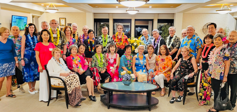 Image: People wearing floral necklaces and floral clothes posing for a photo.