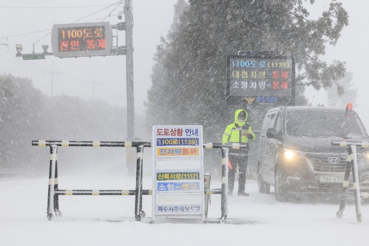 A police officer controls the entry of vehicles at a road amid heavy snowfall on Jeju Island, South Korea, on Jan. 24, 2023.