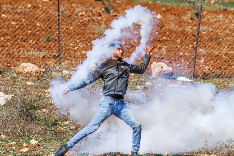 A Palestinian protester throws back a tear gas canister at