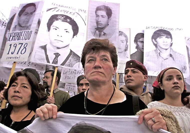 Familiares de personas desaparecidas durante el periodo de contrainsurgencia en México marchan el 2001. Se ve a siete personas portando carteles con las fotos de hombres jóvenes que dicen "Desaparecido en 1978" y "Desaparecido 1975"