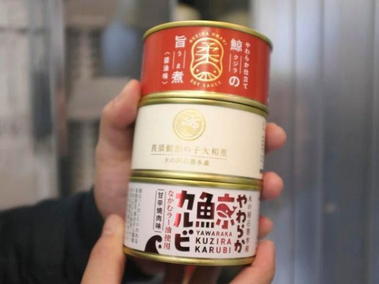 Un cliente muestra latas con carne de ballena compradas en una máquina expendedora.