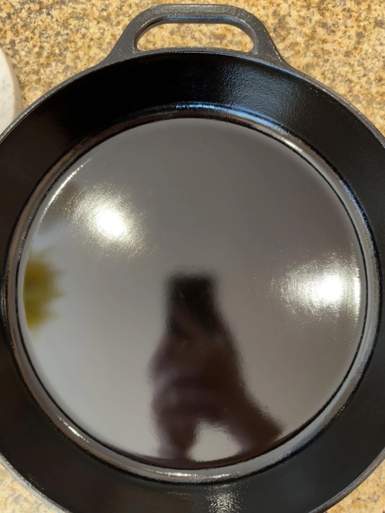Dewey's cast-iron skillet with 80 coats of seasoning and his phone in the reflection.