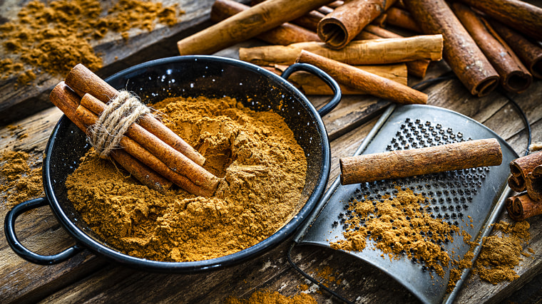 High angle view of a rustic wooden table with cinnamon sticks and ground cinnamon. A small grater is in a container filled with ground cinnamon. Predominant color is brown. High resolution 42Mp studio digital capture taken with SONY A7rII and Zeiss Batis 40mm F2.0 CF lens