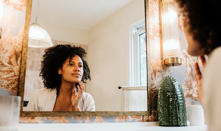 A beautiful woman examines her skin in a bathroom mirror.
