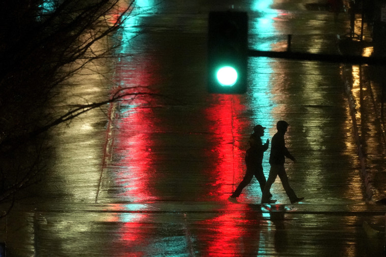 Personas cruzan una calle resbaladiza por la lluvia en el centro de Kansas City, Missouri, mientras una tormenta eléctrica pasaba por la zona, a última hora del lunes 2 de enero de 2023.