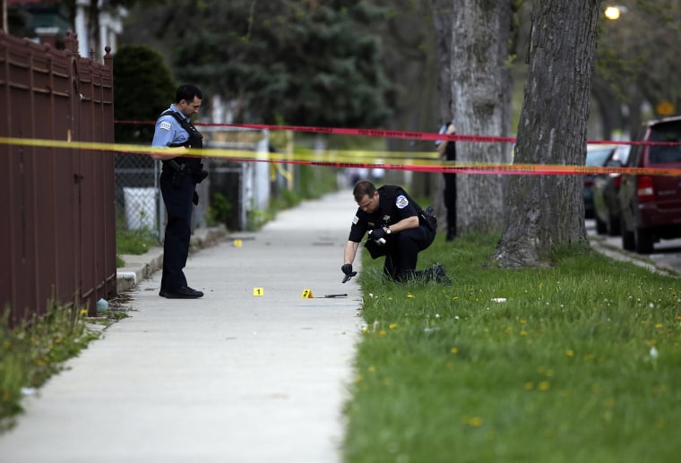 A Chicago Police officer watches as a evidence technician officer investigates a gun at a crime scene in Chicago