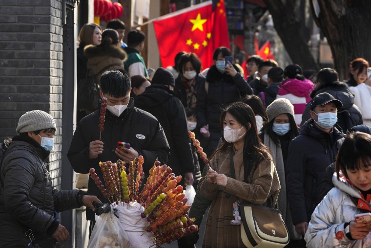 People buy sugar-coated Chinese haws as visitors tour a shopping street near the Drum Tower in Beijing, Monday, Jan. 30, 2023. Chinese people are enjoying the Lunar New Year and visiting various tourist sites in cities around China following the lifting last month of draconian COVID-19 restrictions, allowing a return to many aspects of normal life. (AP Photo/Andy Wong)