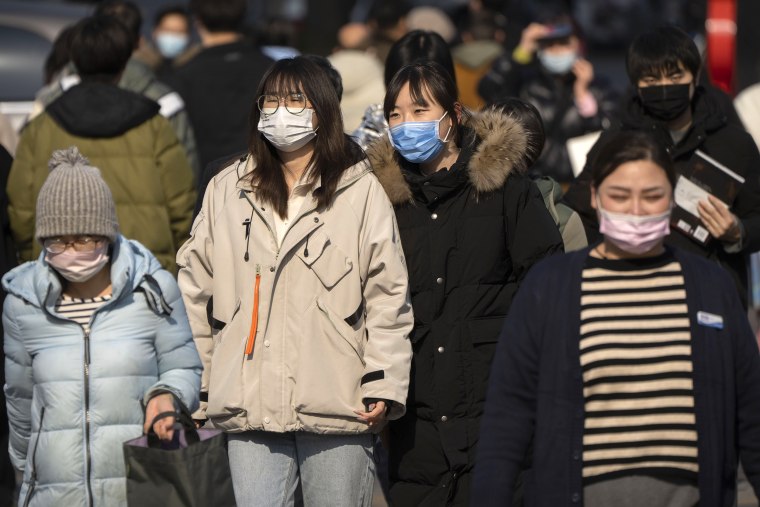 People wearing face masks walk across an intersection in Beijing, Tuesday, Feb. 7, 2023.