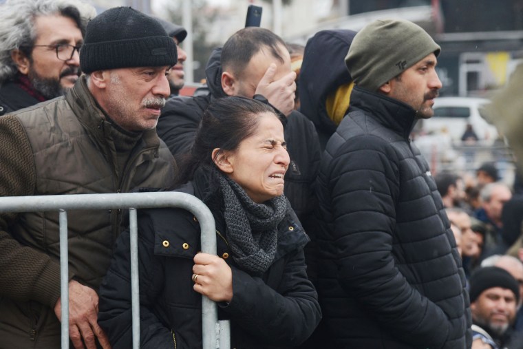 A woman reacts as people watch rescue personnel search for victims and survivors through the rubble of buildings in Kahramanmaras, Turkey on Tuesday.