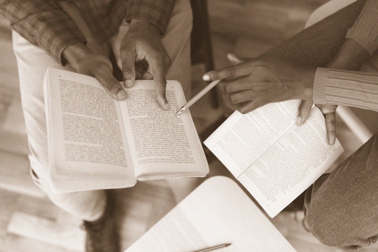 Overhead detail photo of black students analyzing a book.