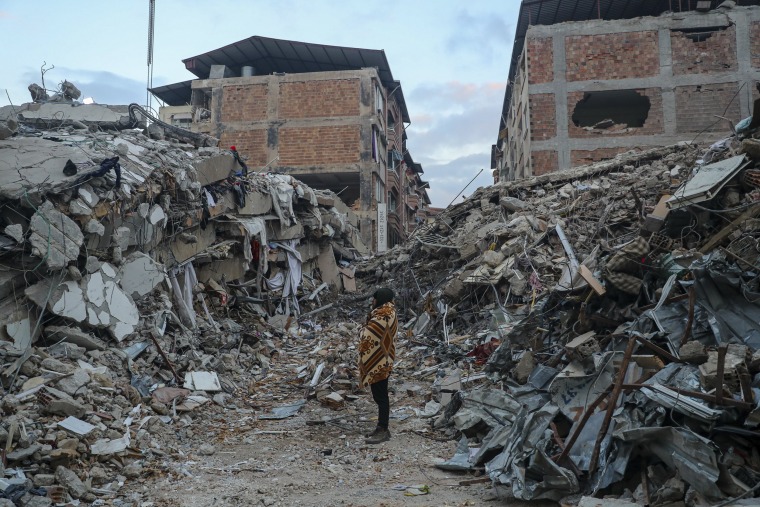 A woman stands among rubble from collapsed buildings in Hatay, Turkey