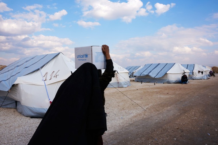 A Syrian woman carries a box of aid at a temporary camp in the village of al-Hamam in northwest Syria on Saturday. 
