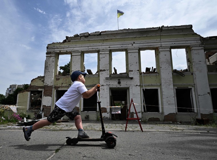 A boy ride his scooter in front of the destroyed building in Okhtyrka, Ukraine,